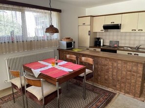 Een keuken met een eettafel, stoelen, een hanglamp en een magnetron.