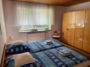 Une chambre avec deux lits, une fenêtre avec des rideaux, un radiateur et des armoires en bois.