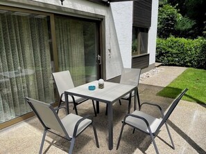 Een terras met een tafel en stoelen, een schuifpui en een kleine tuin.