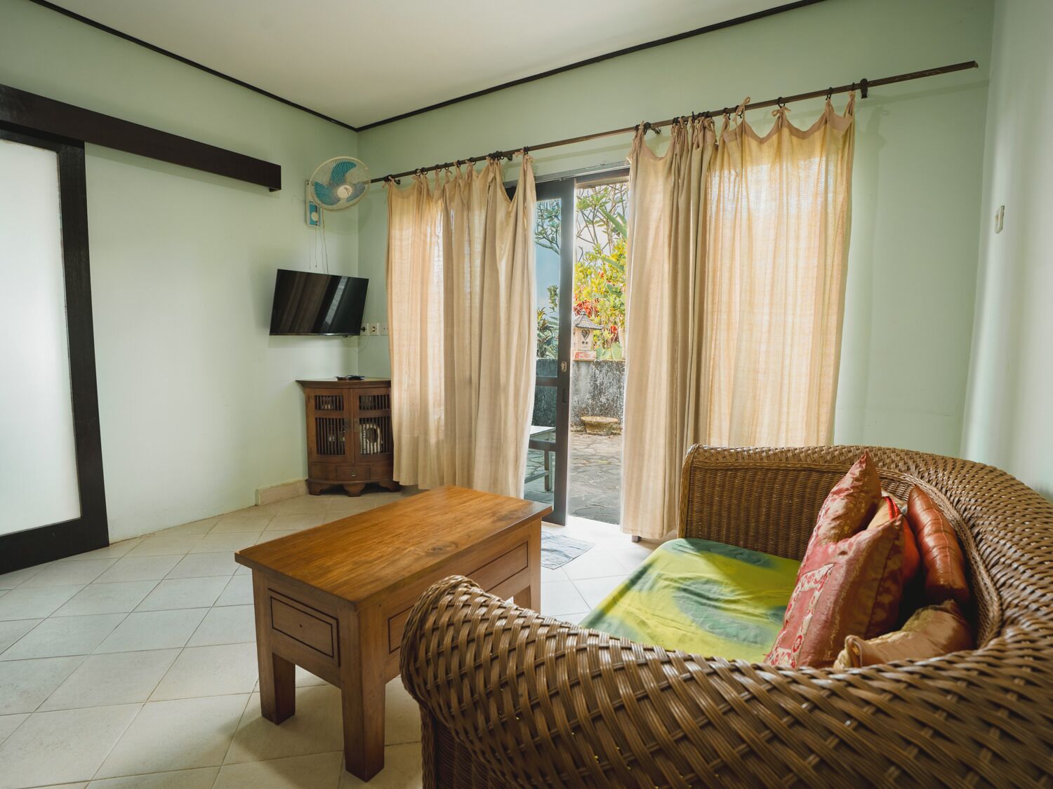 A room with a wooden table, wicker sofa, and a television on the wall.
