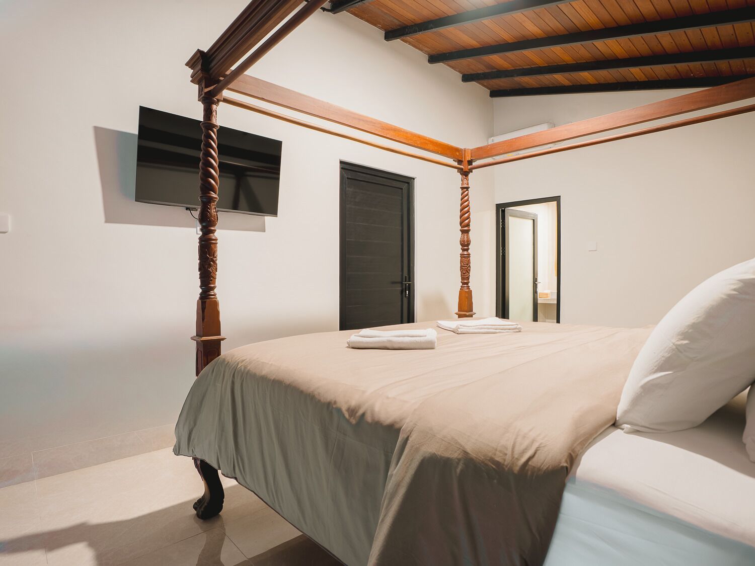 Un dormitorio con cama con dosel, una televisión de pantalla plana y una puerta que da a otra habitación.