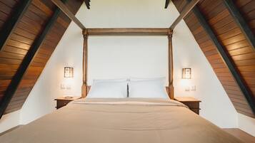 Une pièce aux hauts plafonds, avec un grand lit placé au centre, sous une structure en poutres de bois, et de chaque côté, deux tables de chevet avec des lampes.