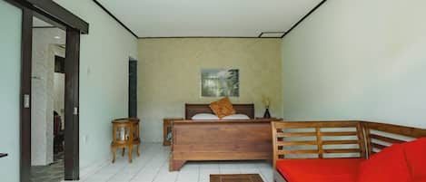 Una habitación con una cama, un banco de madera, una mesita pequeña y un sofá rojo.
