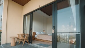 Ein Schlafzimmer mit einem Bett, einem Nachttisch und einem Tisch mit Stühlen. Ein Glasbalkon führt auf einen Balkon.
