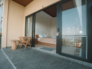 A bedroom with a bed, a nightstand, and a table with chairs. There is a sliding glass door leading to a balcony. - Pacung Indah Hotel & Restaurant (Baturiti)
