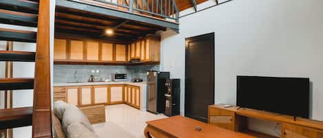 A spacious living area with a high ceiling, wooden beams, a built-in kitchen, and a flat-screen TV.