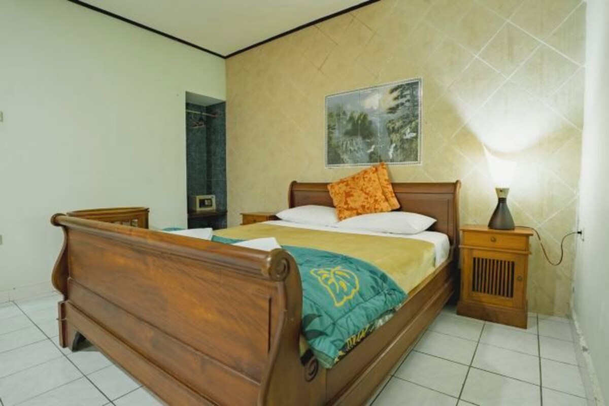 Une chambre à coucher avec un lit en bois, une table de chevet, une lampe fixée au mur et un tableau.