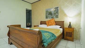 Un dormitorio con una cama de madera, una mesita de noche con lámpara, un cuadro en la pared y suelo de baldosas.