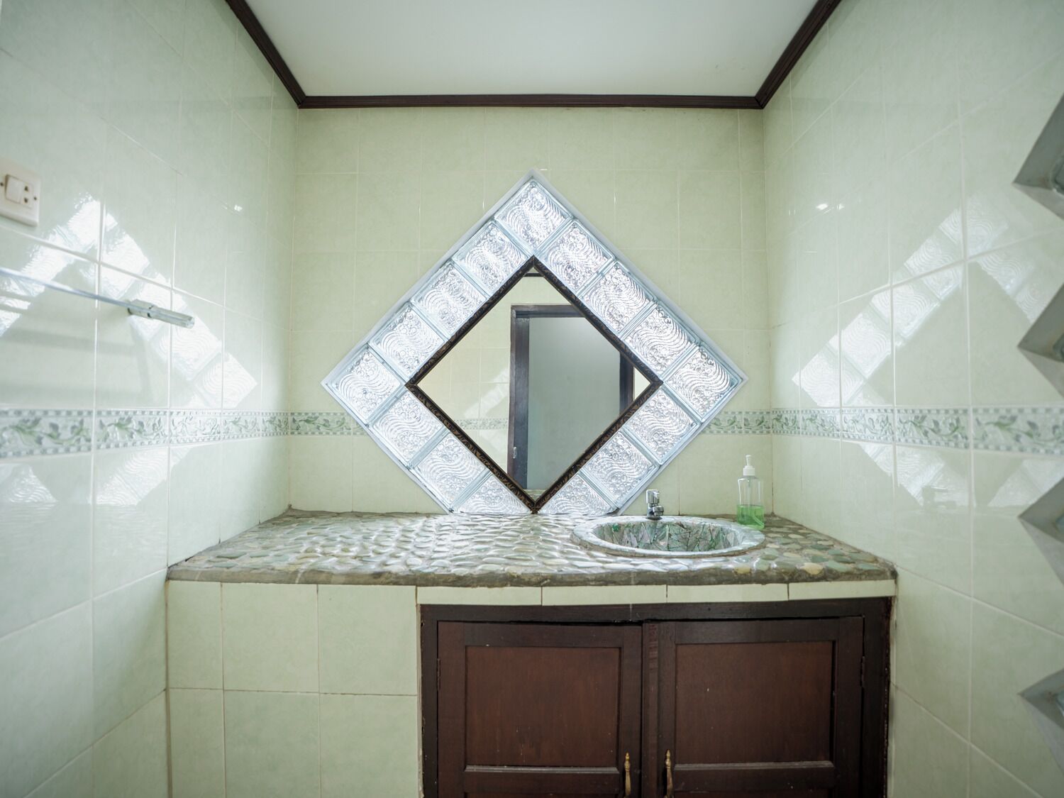 A bathroom with a tiled wall, a diamond-shaped mirror, a sink, and a cabinet.
