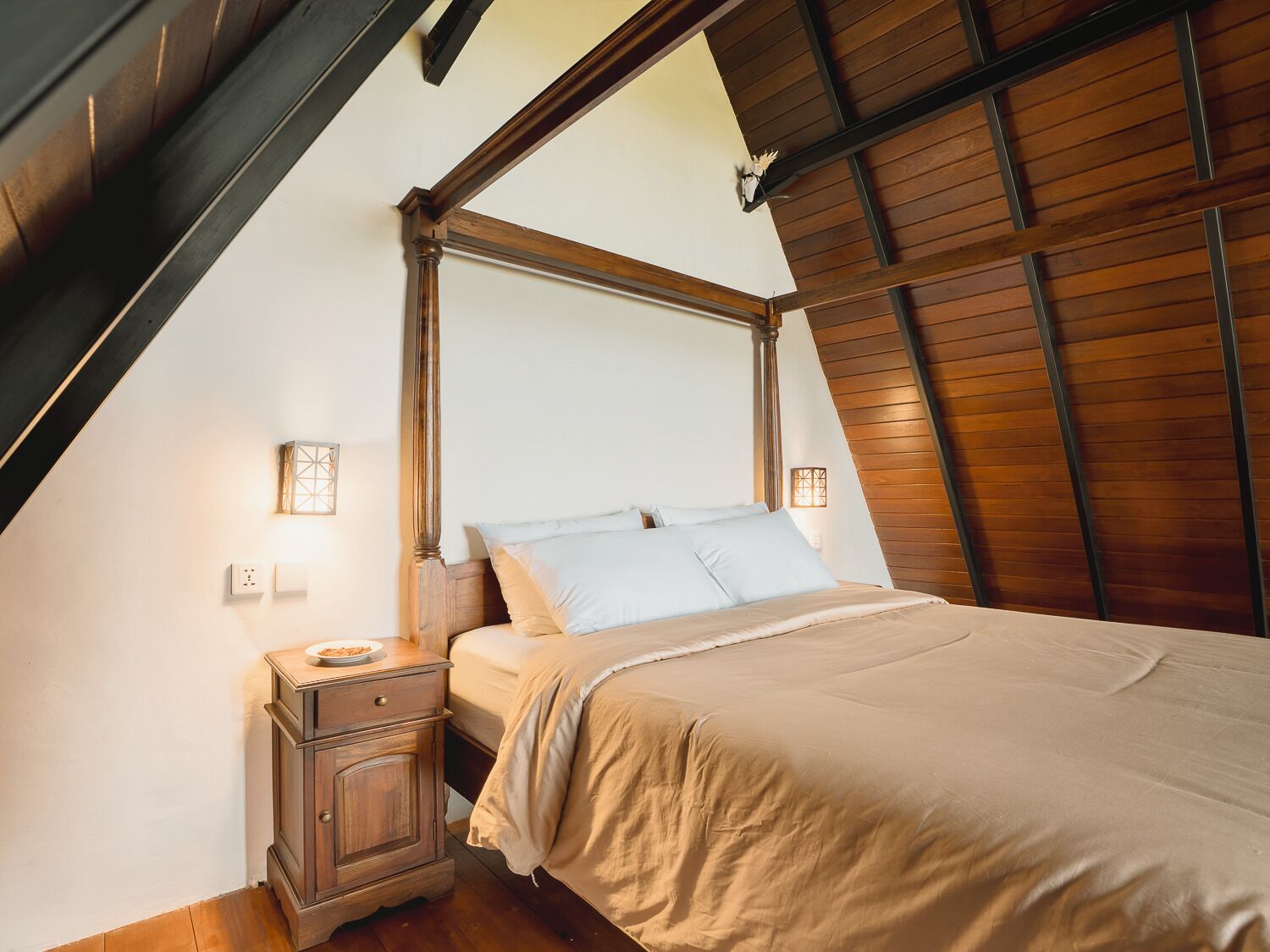 A bedroom with a sloped ceiling, a wooden headboard, a bedside table, and a bed with a beige bedspread.