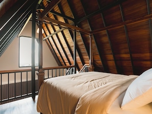 Une chambre avec un plafond en pente, des poutres en bois, un lit avec une literie blanche et une vue sur l’extérieur.