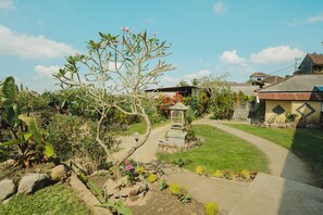 A garden pathway leading to a house with a thatched roof, surrounded by lush greenery and flowering plants. - Pacung Indah Hotel & Restaurant (Baturiti)