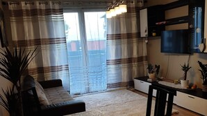Olohuone, jossa on sohva, ruokapöytä tuoleineen, televisio sekä keittiöalue, jossa on myös televisio ja koriste-esineitä.