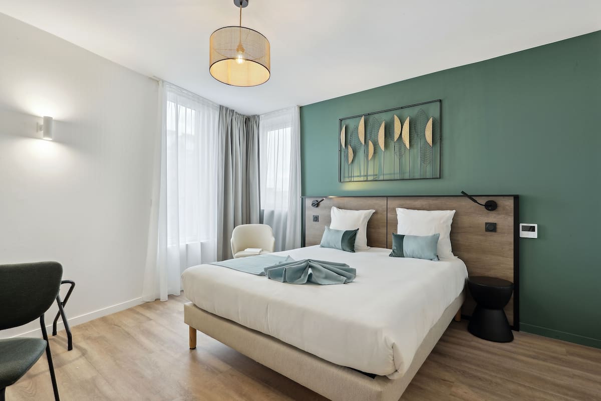 Een moderne hotelkamer met een groot bed, een stoel, een nachtkastje en een kunstwerk aan de muur.