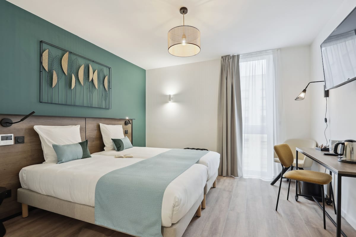Een hotelkamer met een bed, nachtkastjes, een bureau, een stoel, een lamp en een raam met gordijnen.