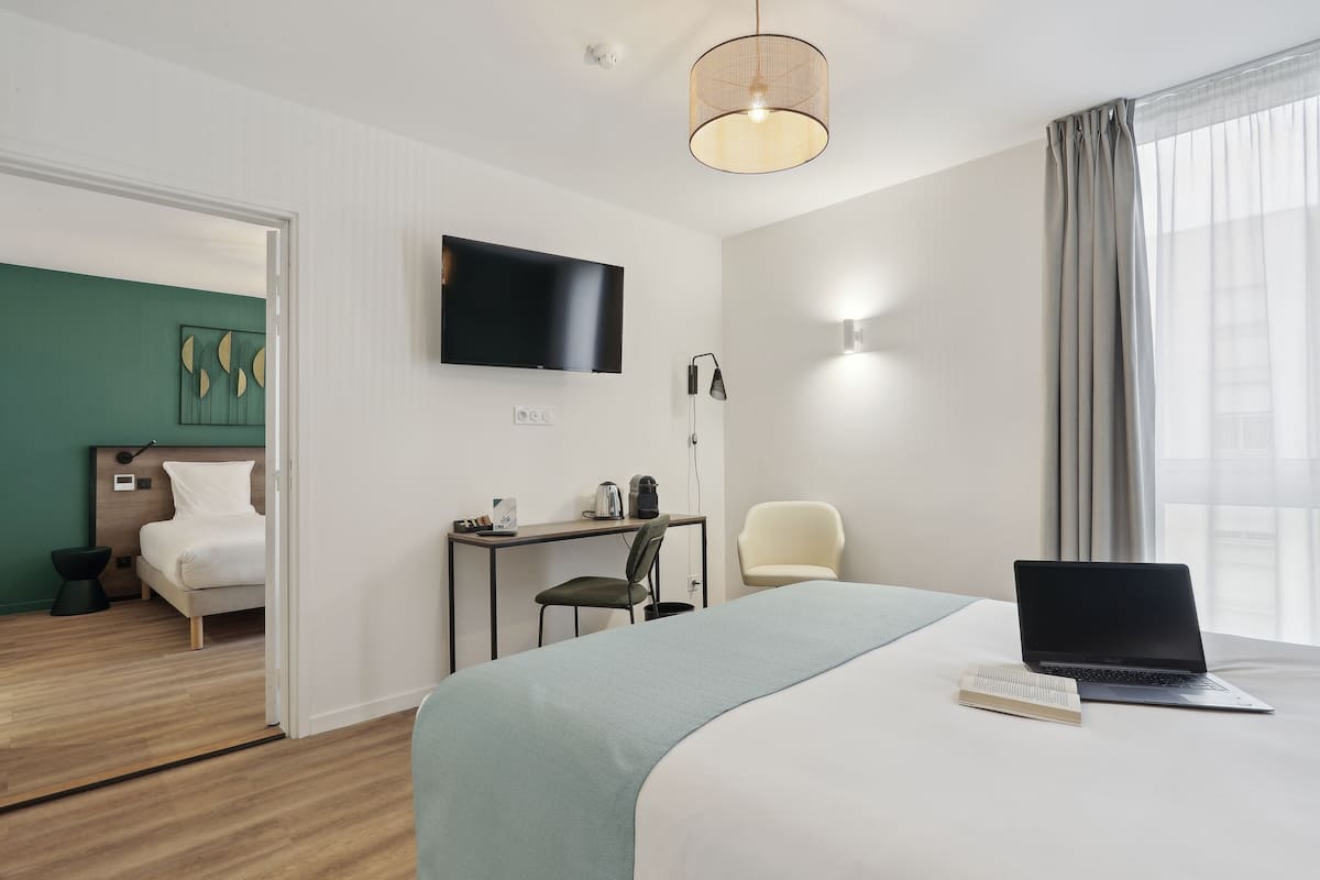 Een moderne hotelkamer met een bed, een bureau met een laptop, een stoel en een televisie.
