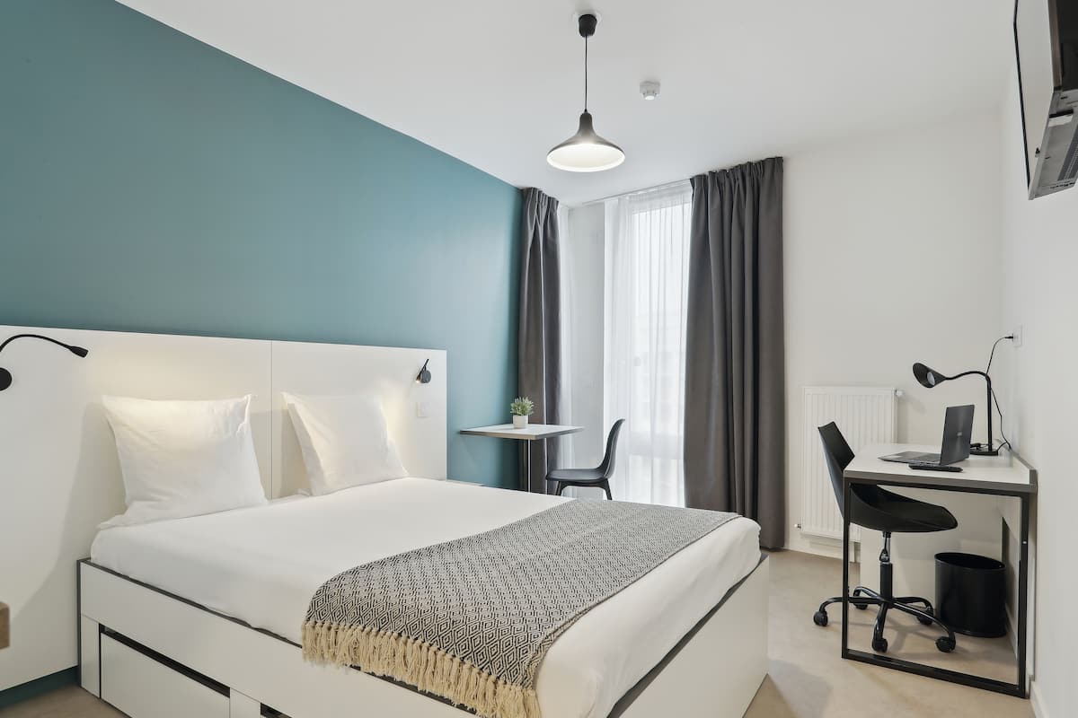 Een moderne hotelkamer met een groot bed, een bureau met een computer en een stoel.