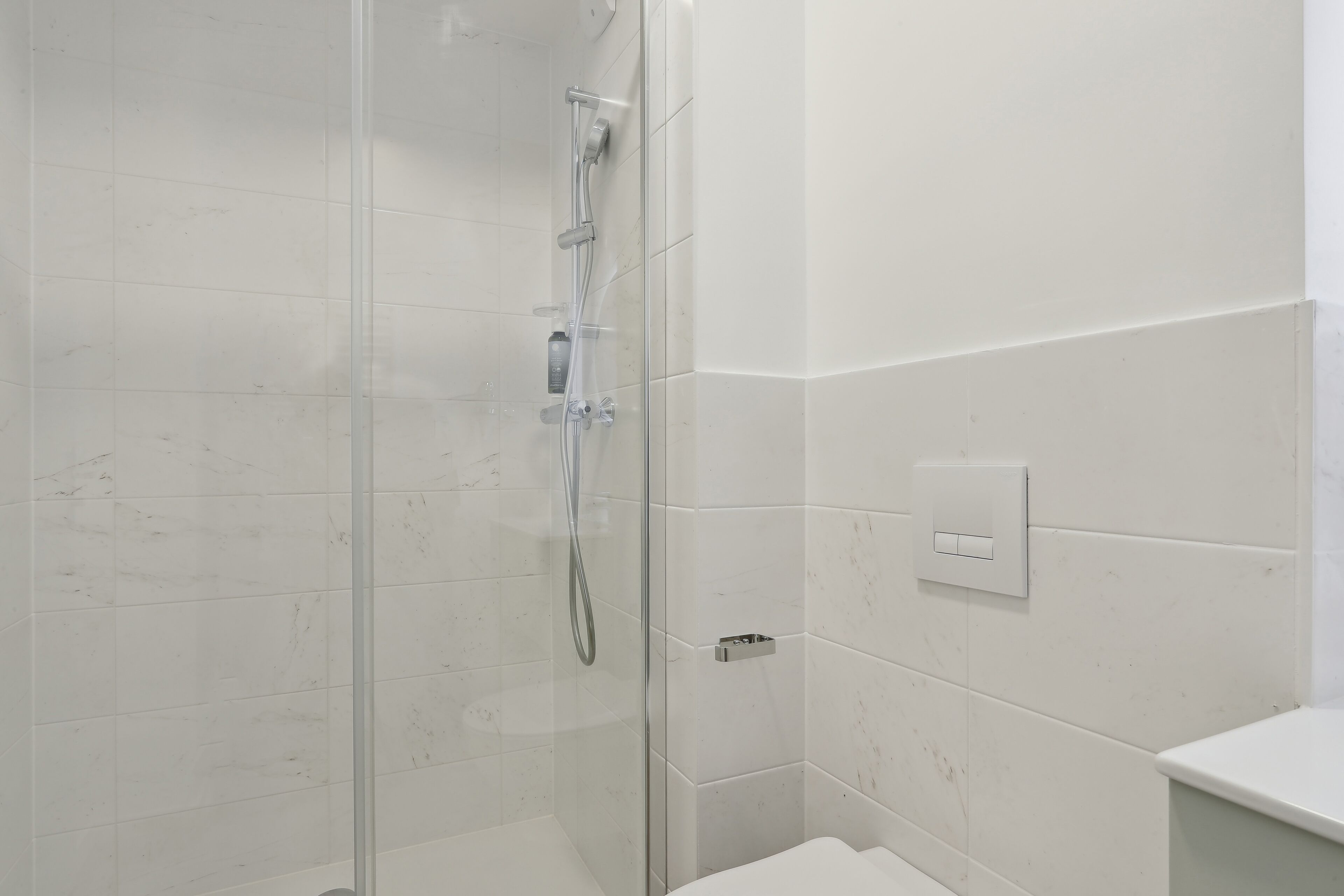 Un baño moderno con cabina de ducha de vidrio, paredes de azulejos blancos y un lavabo blanco.