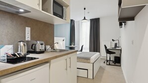 A compact hotel room with a kitchenette, a bed, a desk, and a chair. - All Suites Appart Hôtel | Noisy-le-Grand (Noisy-le-Grand)