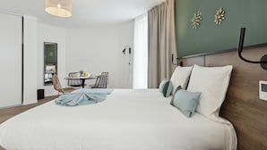 A modern hotel room with a large bed, a dining area with a table and chairs, and decorative wall art. - All Suites Appart Hôtel | Noisy-le-Grand (Noisy-le-Grand)
