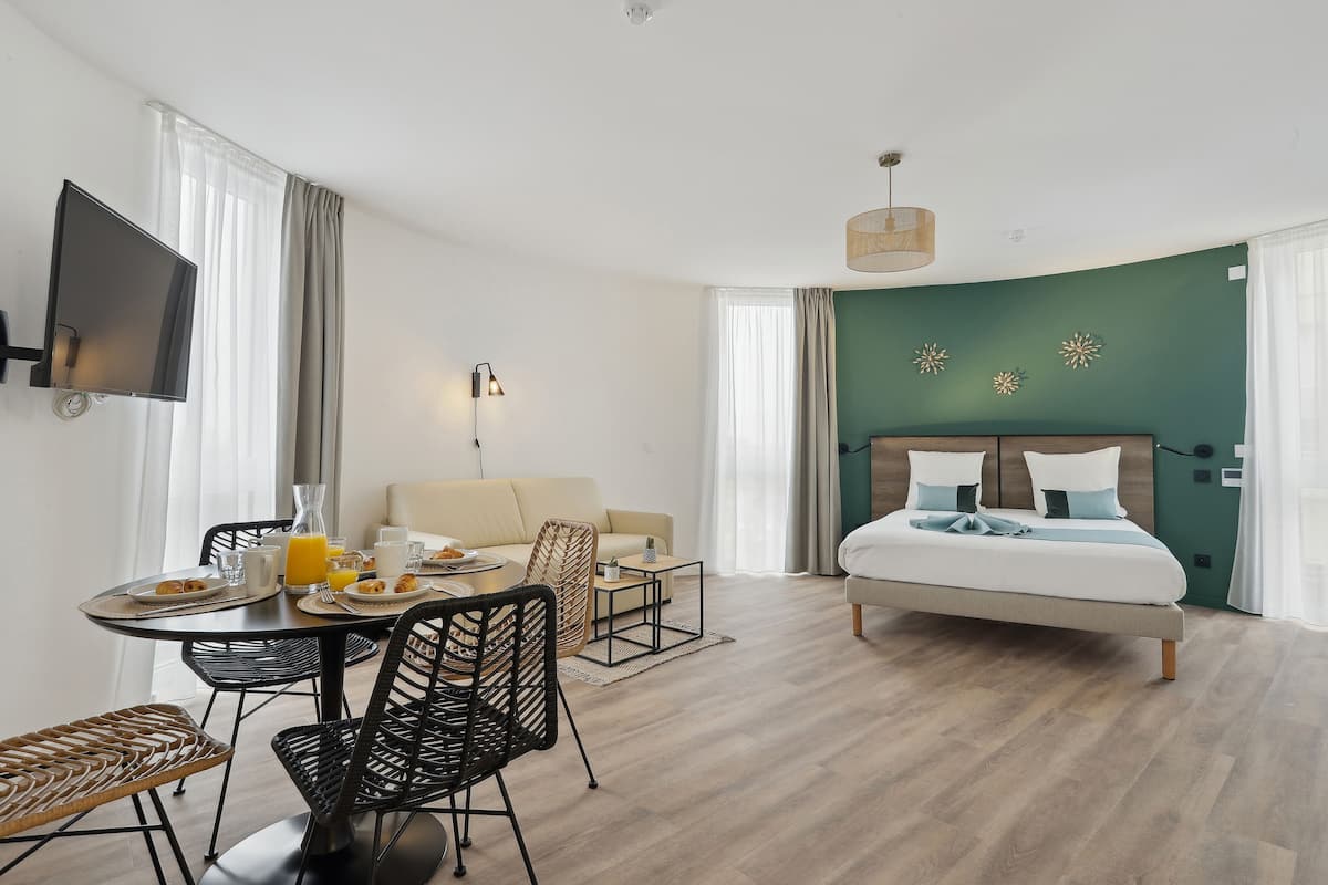 Een moderne hotelkamer met een bed, een zithoek met een tafel en stoelen, een aan de muur bevestigde televisie en een groene accentmuur.