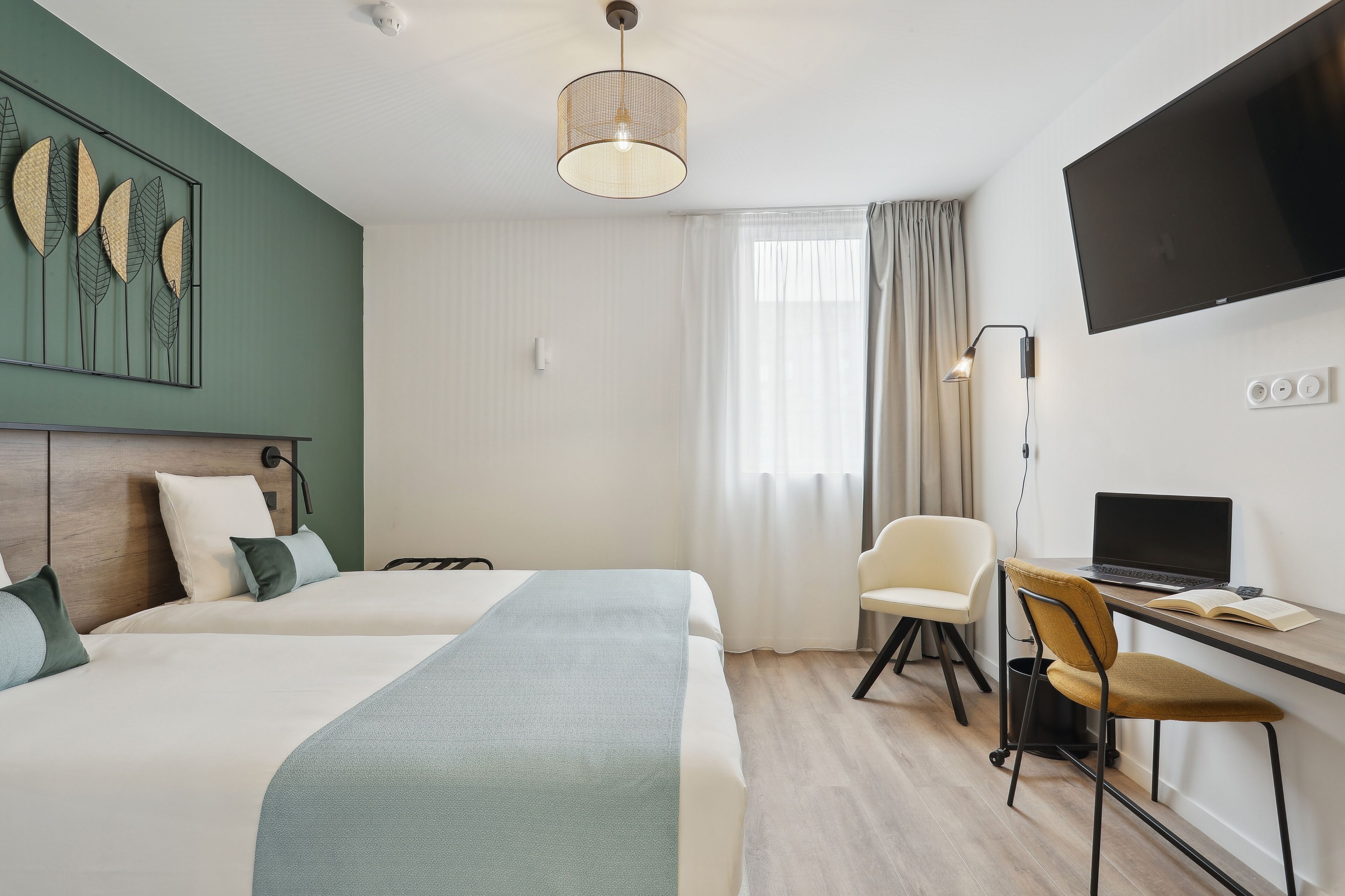 A hotel room with two beds, a desk with a laptop, a TV, and a large window with curtains.