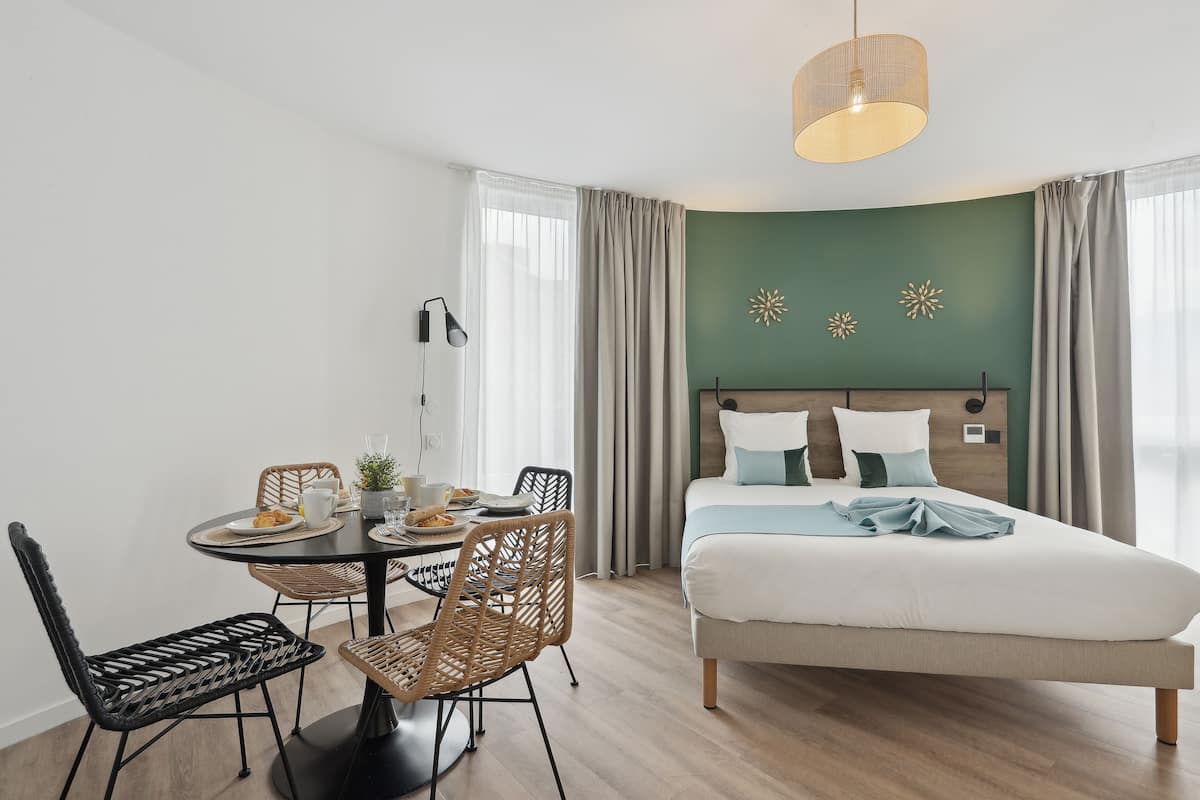 Een moderne slaapkamer met een bed, een eettafel met stoelen en een hanglamp.