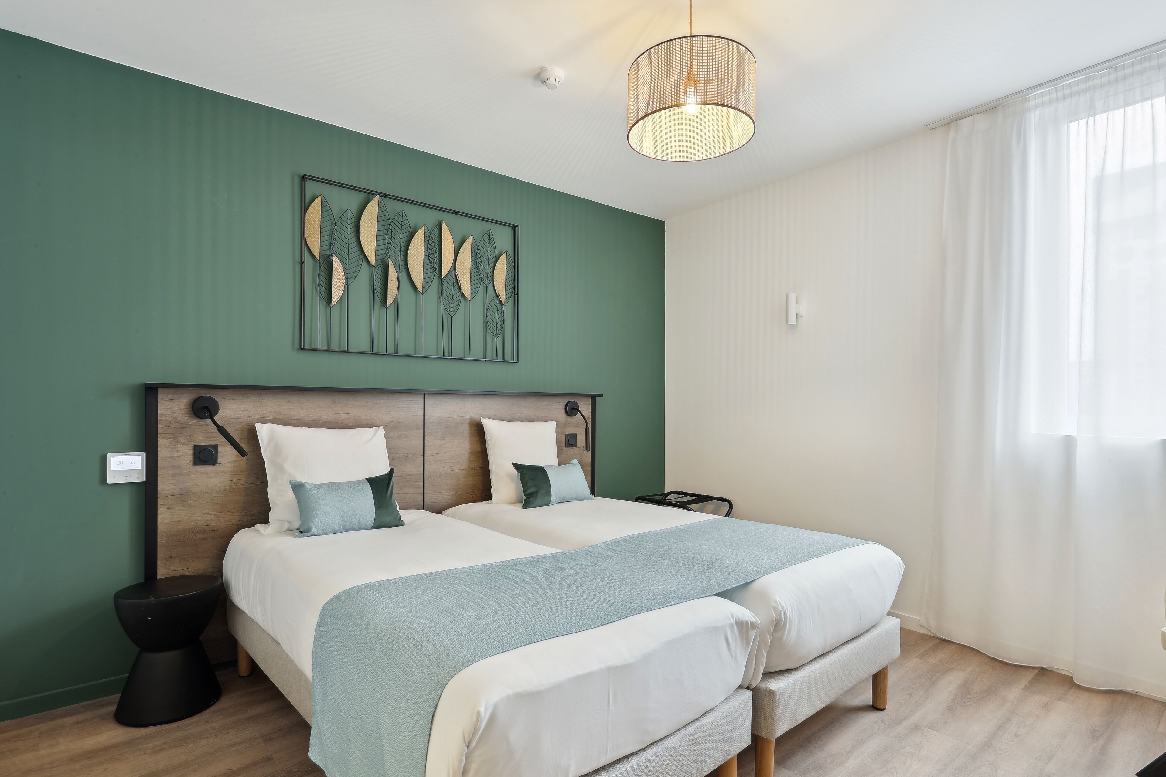 Een moderne slaapkamer met twee bedden, een houten hoofdbord, een kunstwerk aan de muur en een groot raam met gordijnen.