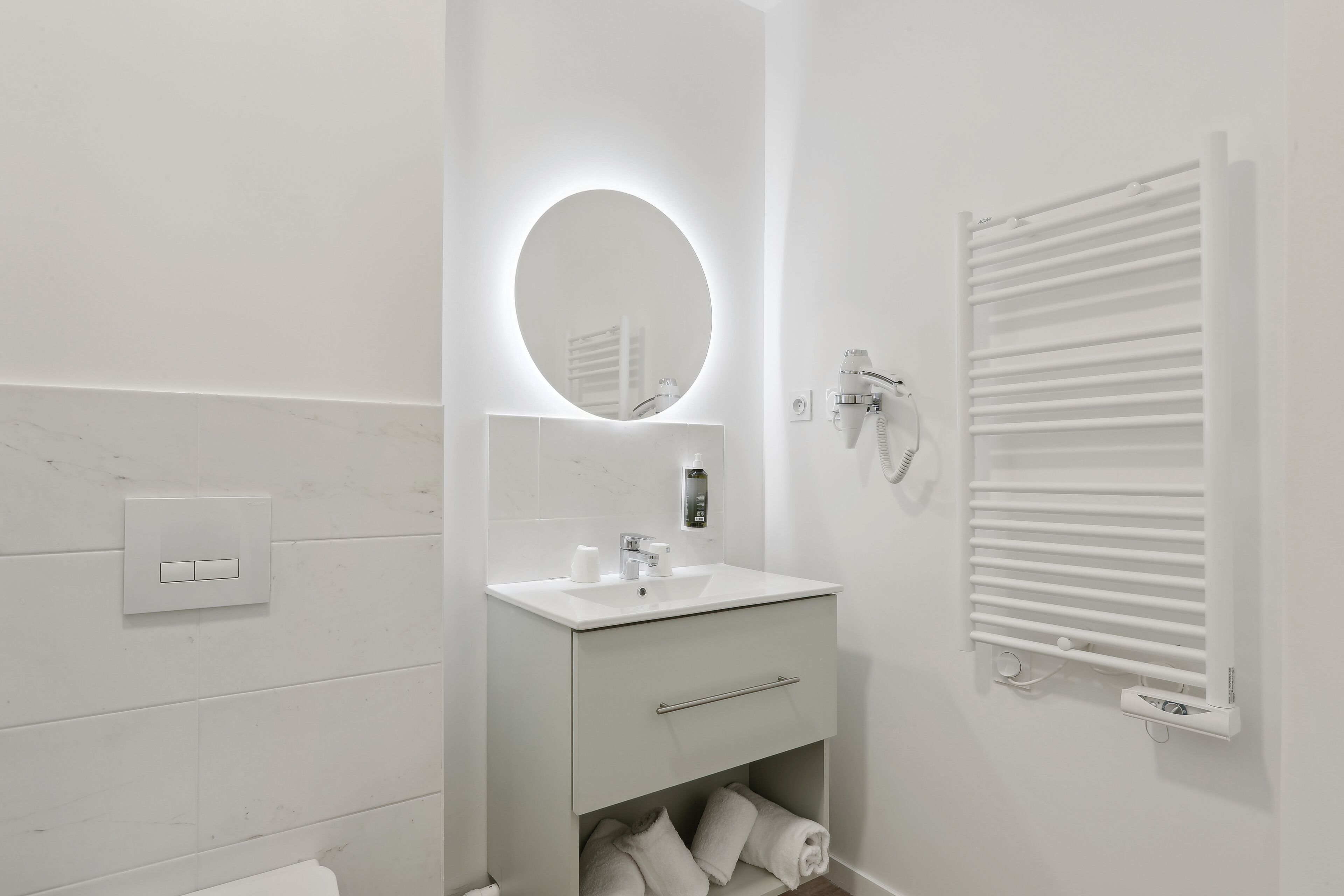 Un baño moderno con un lavabo blanco, espejo y toallero.