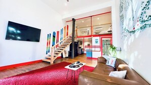A spacious living area with a red carpet, a brown leather sofa, a wooden staircase, and a modern kitchen in the background.