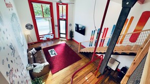 A modern interior with a wooden floor, red accents, a red carpet, a sofa, a TV, and a staircase with a railing.