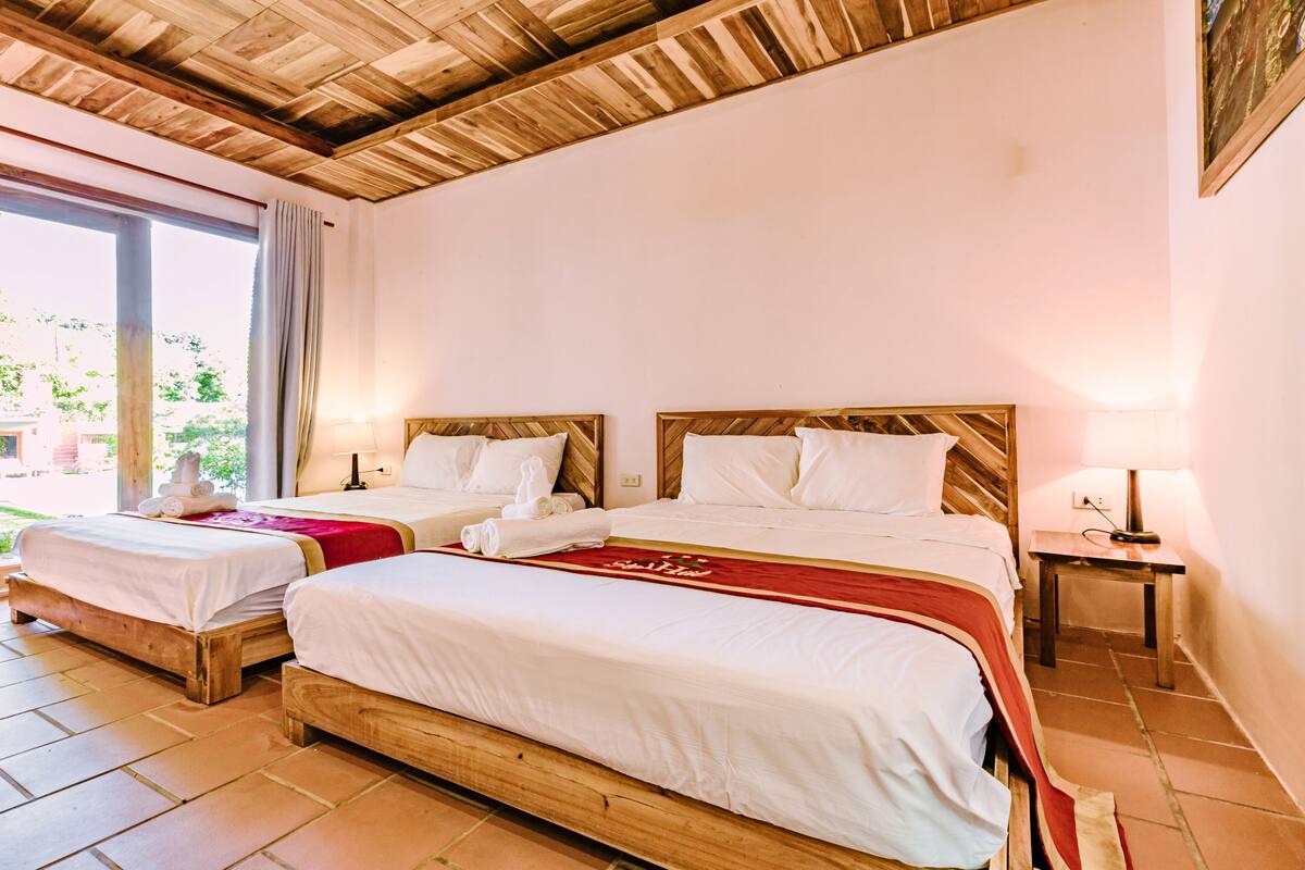 Ein Hotelzimmer mit zwei Holzbettgestellen, einer roten Bettdecke und einer Holzbalkendecke.