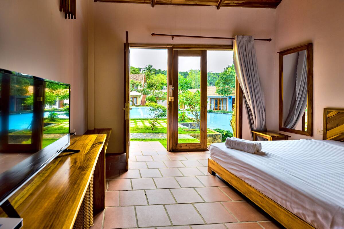 Ein Hotelzimmer mit Bett, Fernseher und Blick auf einen Pool und Grünflächen.