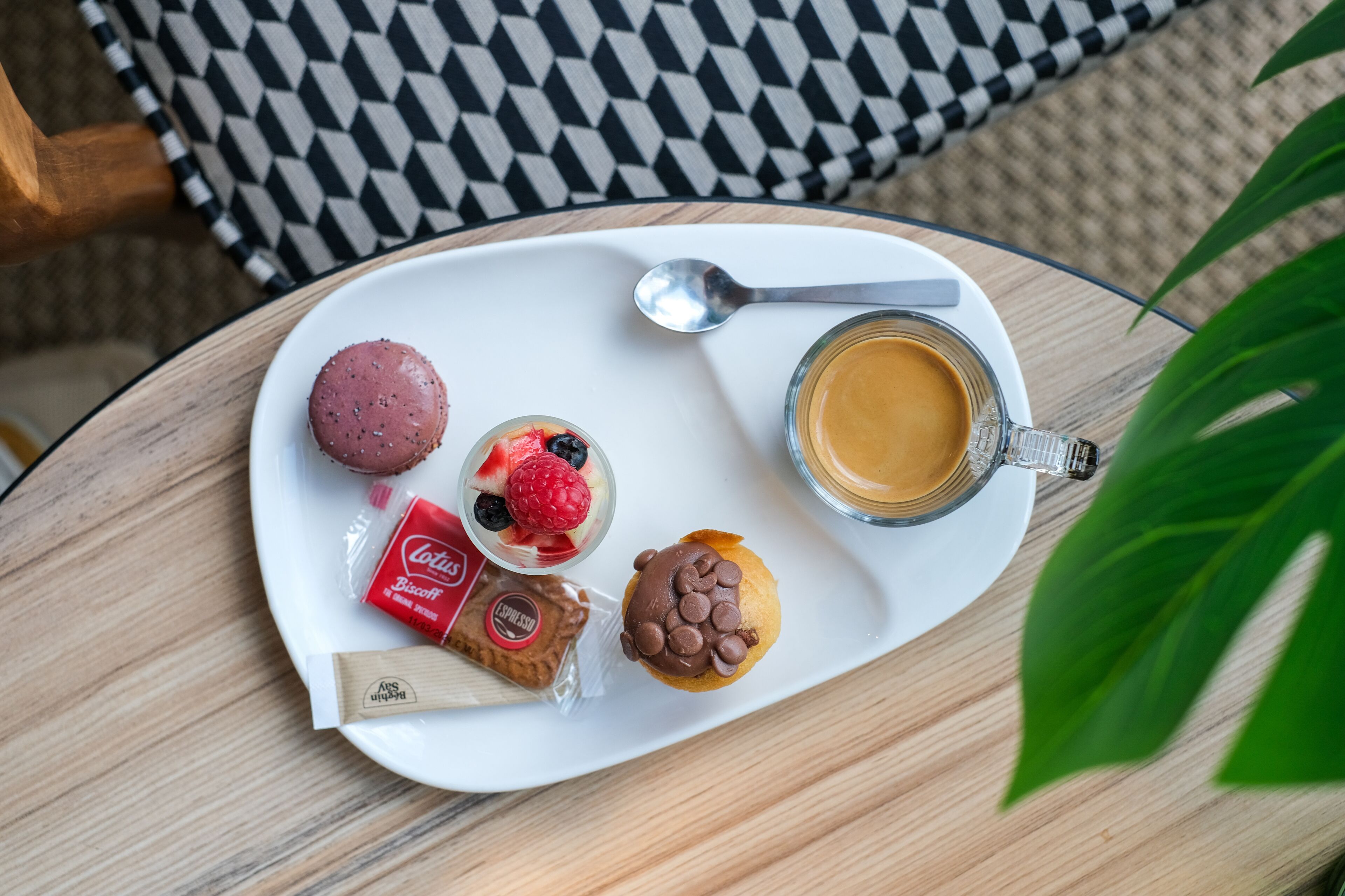 A white plate with a variety of snacks and a cup of coffee on a round table.