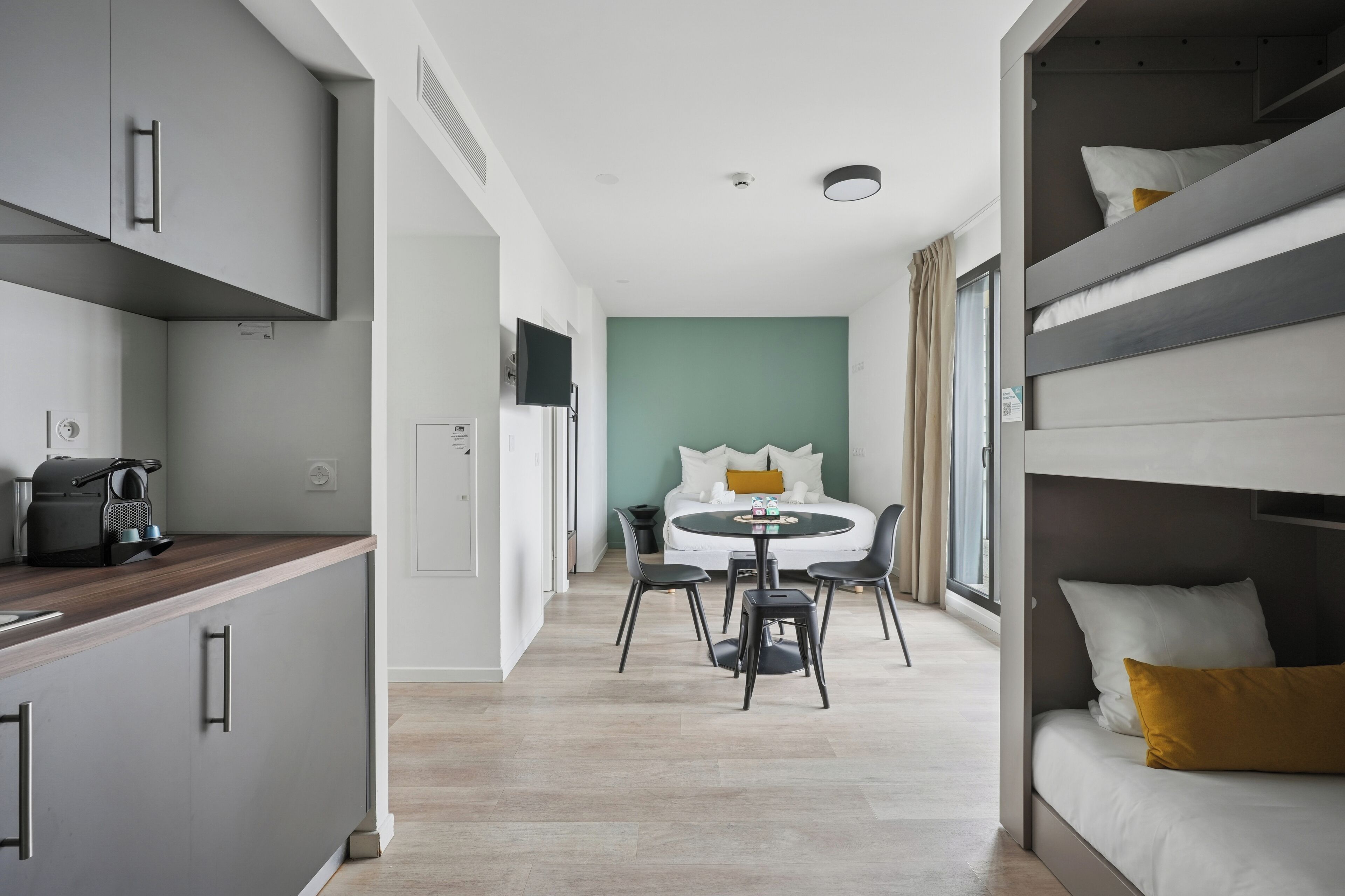 A modern hotel room with a kitchenette, a dining area, and a bed with bunk beds.