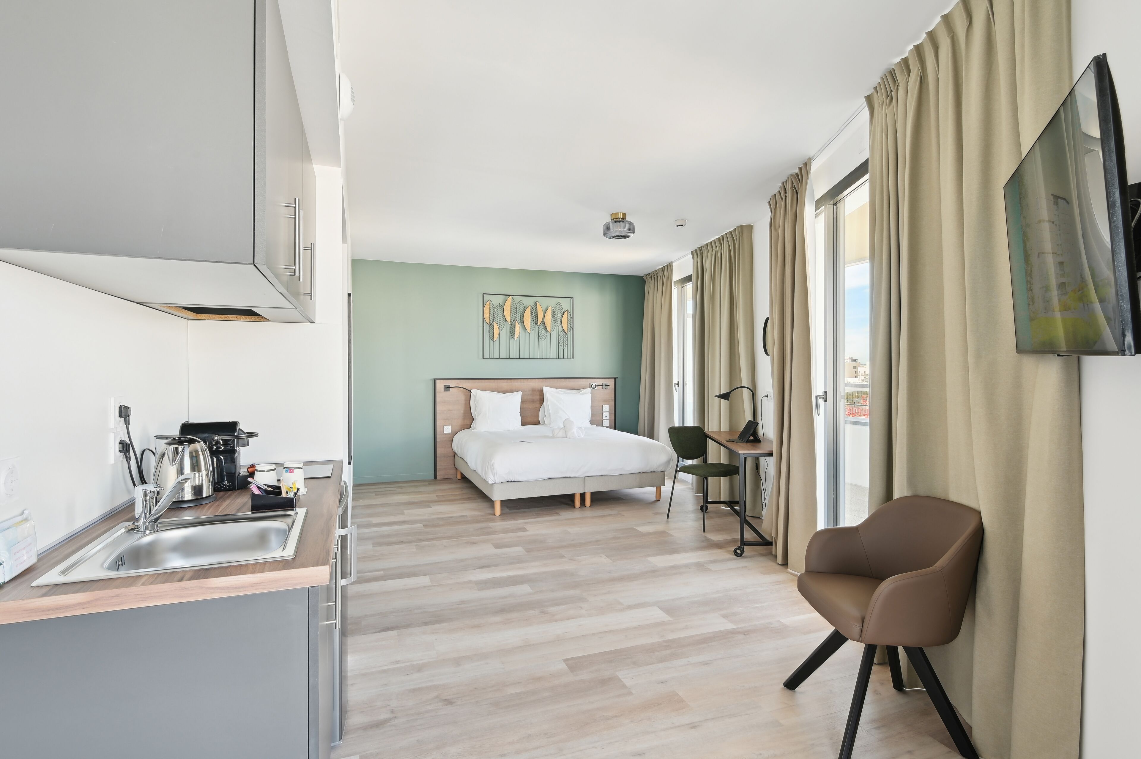 A modern hotel room with a kitchenette, a bed, a desk, and a chair.