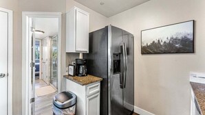 Eine kleine Küche mit einem Edelstahl-Kühlschrank, einer Kaffeemaschine und einem Mülleimer.