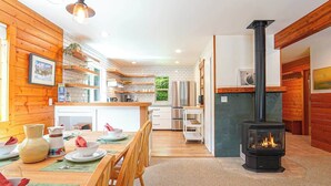 Una cocina moderna con una isla central, un comedor con sillas de madera y un estufa de leña en color negro.