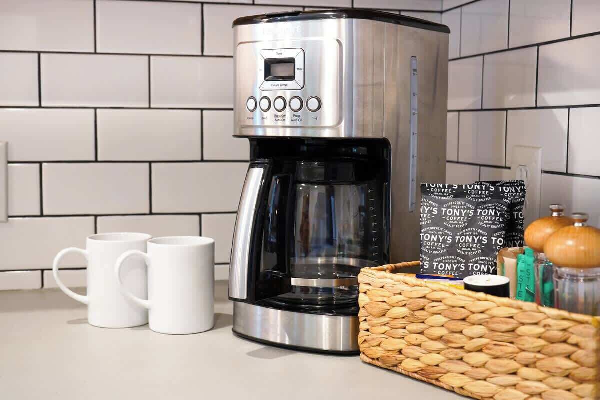 Une cuisine équipée d’une machine à café, de deux tasses blanches, d’un panier rempli de grains de café et d’un sac de café.