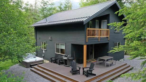 Una cabaña de dos pisos con terraza, mobiliario exterior y un jacuzzi.