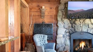 Una habitación acogedora con chimenea de piedra, un ventanal con vistas a la montaña, un sillón capitonado y un panel decorativo en la pared.