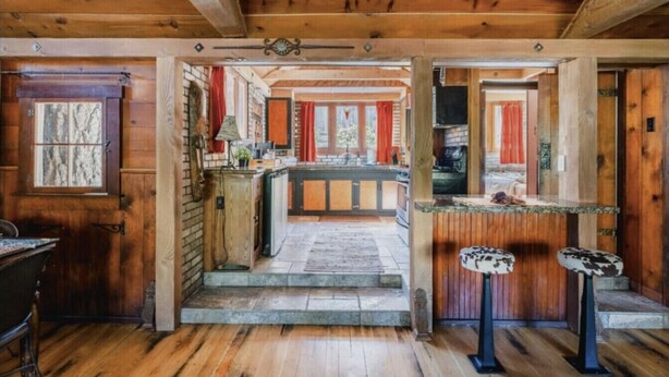Un interior rústico de madera con zona de cocina, vigas de madera y chimenea de piedra.