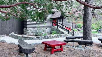 A rustic cabin with a stone foundation, a wooden deck, and a red bench.