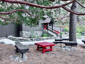 Una cabaña rústica con base de piedra, una terraza de madera y un banco rojo.