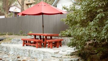 A red picnic table with an umbrella, set on stone steps in a backyard with a wooden fence and a house in the background.