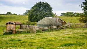 A rustic farm setting with a green-roofed greenhouse, wooden structures, and a fenced area with a variety of flowers. - Mongolian Yurts Fordhall Organic Farm (Market Drayton)