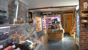 A deli with a glass display case filled with various meats, a brick wall, and a wooden counter with deli items. - Mongolian Yurts Fordhall Organic Farm (Market Drayton)
