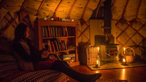 A cozy room with a large bookshelf, a fireplace, and a person reading. - Mongolian Yurts Fordhall Organic Farm (Market Drayton)