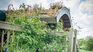 A wooden structure with a green roof, a wooden bench with a sign, and a garden area with various plants and flowers. - Mongolian Yurts Fordhall Organic Farm (Market Drayton)