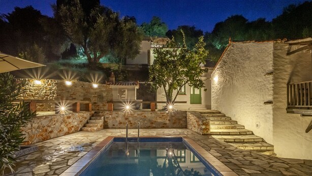 A swimming pool with stone steps leading up to it, surrounded by a white wall and a tree.